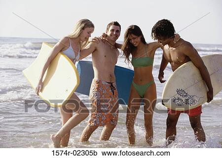 Stock Image - Two teenage couples standing on the beach holding boogie boards. Fotosearch