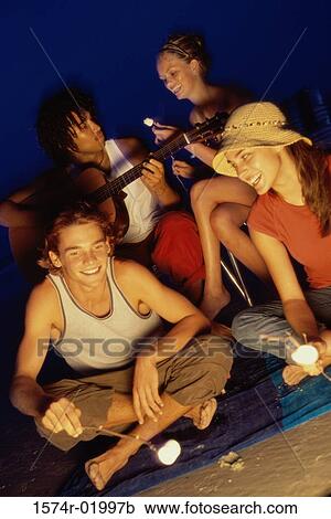 Stock Image - Two young couples sitting by a campfire toasting marshmallows. Fotosearch