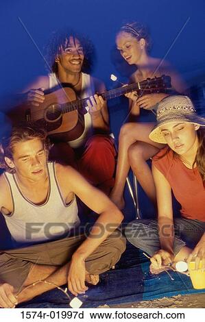 Two young couples sitting by a campfire toasting marshmallows View Large Photo Image Stock Image - Two young couples sitting by a campfire toasting marshmallows. Fotosearch