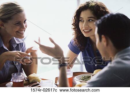 Stock Image - Two young women and a young man sitting in a restaurant. Fotosearch