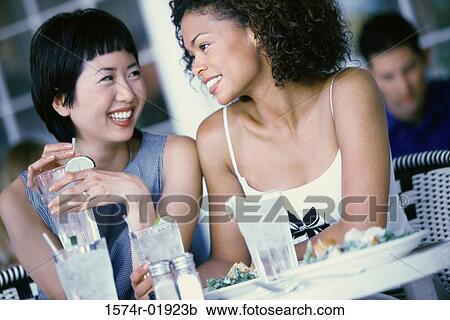 Two young women seated at a table smiling View Large Photo Image Stock Image - Two young women seated at a table smiling. Fotosearch