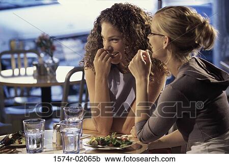 Stock Image - Two young women sitting together at a table in a restaurant. Fotosearch