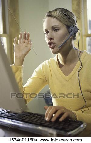 Young businesswoman talking on a headset using a computer in an office View Large Photo Image Stock Image - Young businesswoman talking on a headset using a computer in an office. Fotosearch