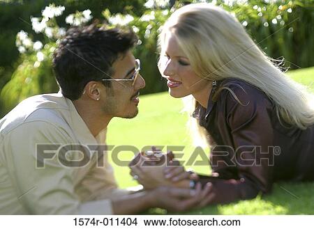 Young couple lying together on a lawn looking at each other View Large Photo Image Picture - Young couple lying together on a lawn looking at each other. Fotosearch