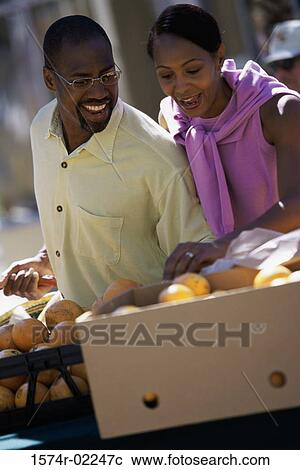 Stock Image - Young couple picking oranges from a shop in a market. Fotosearch