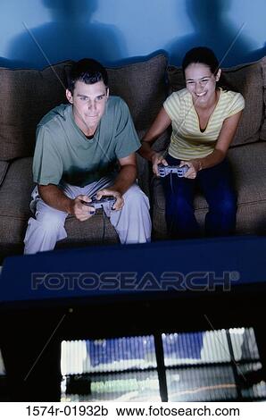 Stock Image - Young couple sitting on a couch playing video games. Fotosearch