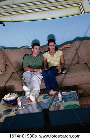 Young couple sitting on a couch watching television View Large Photo Image Stock Image - Young couple sitting on a couch watching television. Fotosearch