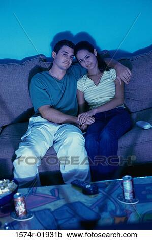Stock Image - Young couple sitting on a couch watching television. Fotosearch