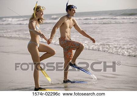 Stock Image - Young couple walking on the beach wearing snorkels and flippers. Fotosearch