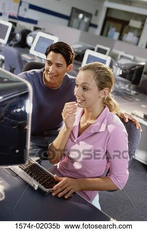 Stock Image - Young man and a young woman looking at a computer monitor. Fotosearch