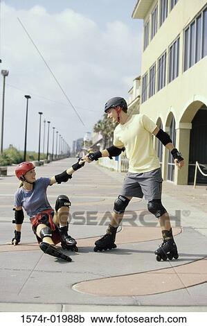 Stock Image - Young man helping up a young woman on inline skates. Fotosearch