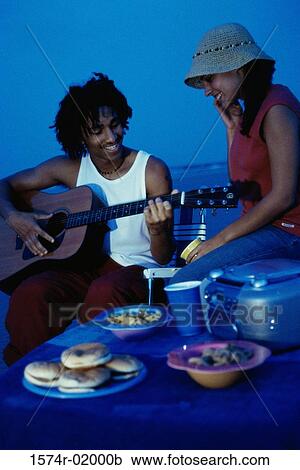 Stock Image - Young man playing a guitar on the beach with a young woman. Fotosearch