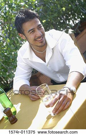 Stock Photography - Young man sitting outdoors holding a glass of water. Fotosearch