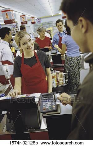 Stock Image - Young man using a credit card machine at a checkout counter in a supermarket. Fotosearch