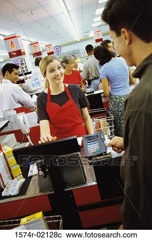 Stock Image - Young man using a credit card machine at a checkout counter in a supermarket. Fotosearch