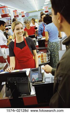 Stock Image - Young man using a credit card machine at a checkout counter in a supermarket. Fotosearch