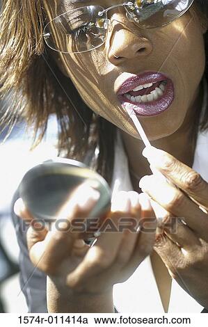 Stock Image - Young woman applying lipstick outdoors. Fotosearch