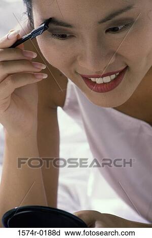 Young woman applying make-up in a mirror View Large Photo Image Stock Image - Young woman applying make-up in a mirror. Fotosearch