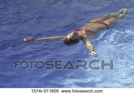 Stock Image - Young woman floating in a swimming pool. Fotosearch