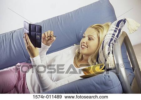 Stock Photo - Young woman lying on a couch writing in a planner. Fotosearch