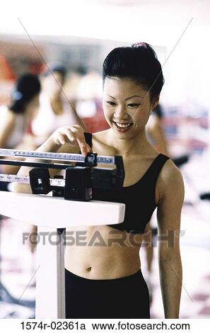 Stock Image - Young woman standing on a weight scale. Fotosearch
