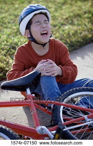 Stock Image - Boy fallen from a bicycle holding his injured knee. Fotosearch