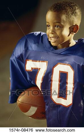Boy in an oversized football uniform holding a ball View Large Photo Image Stock Photograph - Boy in an oversized football uniform holding a ball. Fotosearch