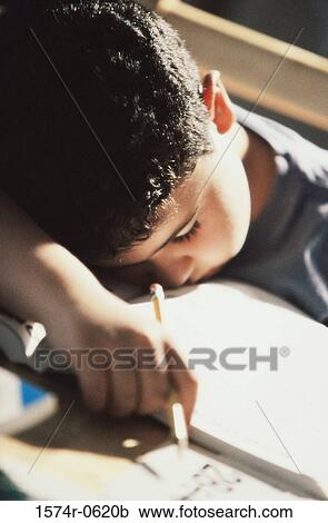Stock Image - Boy sleeping on his books holding a pencil. Fotosearch