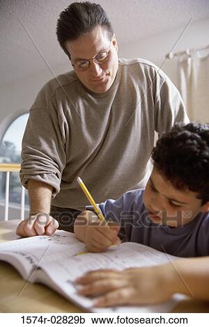 Boy writing in a book with his father standing beside him View Large Photo Image Stock Image - Boy writing in a book with his father standing beside him. Fotosearch