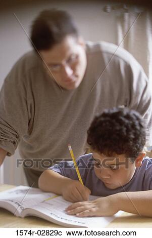 Boy writing in a book with his father standing beside him View Large Photo Image Stock Image - Boy writing in a book with his father standing beside him. Fotosearch