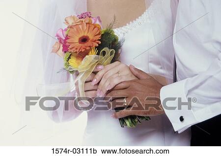 Bride and groom holding a bouquet of flowers together View Large Photo Image Stock Image - Bride and groom holding a bouquet of flowers together. Fotosearch