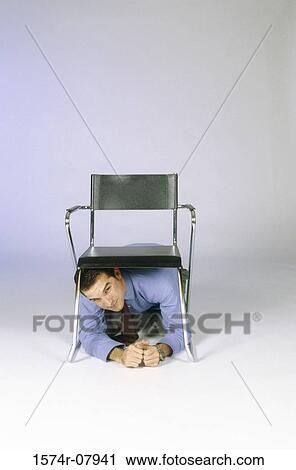 Stock Image - Businessman crouching under a chair. Fotosearch
