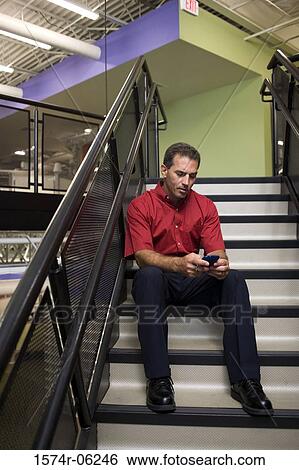 Businessman holding a mobile phone sitting on a staircase View Large Photo Image Stock Photograph - Businessman holding a mobile phone sitting on a staircase. Fotosearch