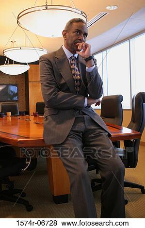 Stock Photo - Businessman leaning against a table in a conference room. Fotosearch