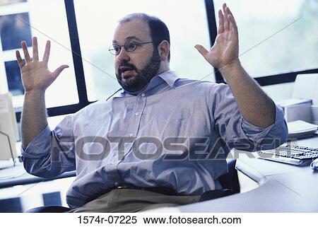 Businessman seated at an office desk with his hands raised View Large Photo Image Stock Photography - Businessman seated at an office desk with his hands raised. Fotosearch
