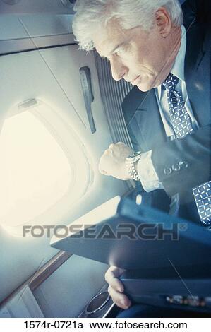 Businessman sitting in an airplane looking at his wristwatch View Large Photo Image Stock Image - Businessman sitting in an airplane looking at his wristwatch. Fotosearch