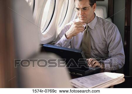 Stock Image - Businessman sitting in an airplane using a laptop. Fotosearch