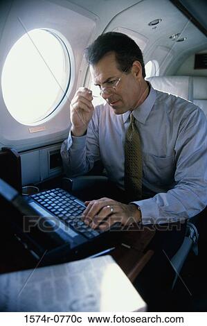 Businessman sitting in an airplane using a laptop View Large Photo Image Stock Image - Businessman sitting in an airplane using a laptop. Fotosearch