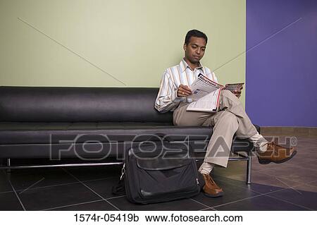Businessman sitting on a couch reading a magazine in an office View Large Photo Image Stock Image - Businessman sitting on a couch reading a magazine in an office. Fotosearch
