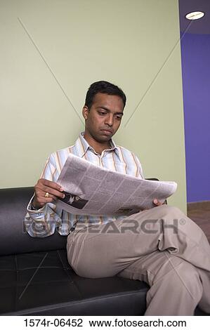 Businessman sitting on a couch reading a newspaper in an office View Large Photo Image Stock Image - Businessman sitting on a couch reading a newspaper in an office. Fotosearch