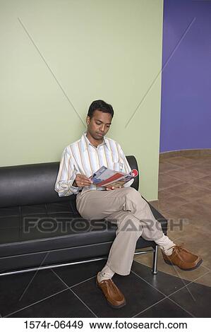 Businessman sitting on a couch reading a magazine in an office View Large Photo Image Stock Photo - Businessman sitting on a couch reading a magazine in an office. Fotosearch