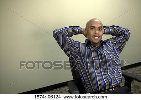 Picture - Businessman sitting with his hands behind his head in an office. Fotosearch
