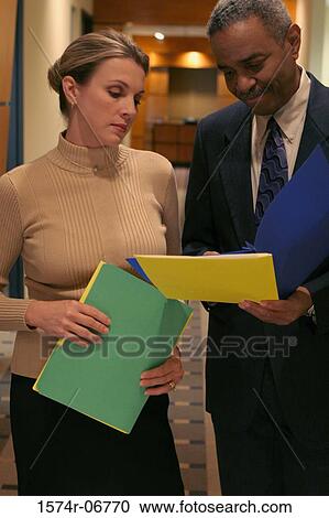 Stock Image - Businessman standing in a corridor talking to a businesswoman. Fotosearch