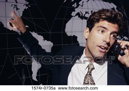 Stock Image - Businessman talking on a mobile phone while pointing to a world map. Fotosearch
