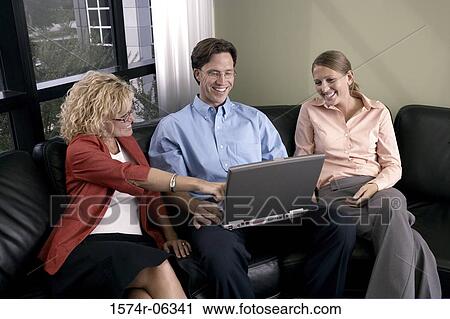 Stock Image - Businessman using a laptop with two businesswomen sitting beside him. Fotosearch