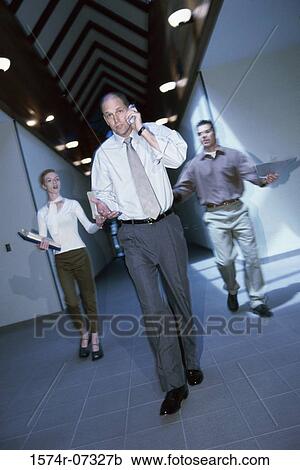 Stock Image - Businessman walking in a corridor and talking on a mobile phone. Fotosearch