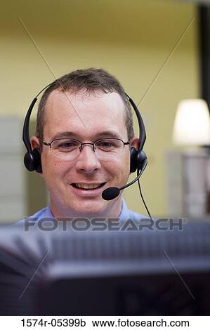 Stock Image - Businessman wearing a headset in an office. Fotosearch