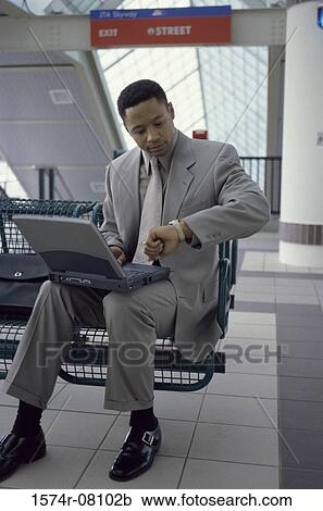 Businessman with a laptop sitting and looking at his wristwatch View Large Photo Image Stock Image - Businessman with a laptop sitting and looking at his wristwatch. Fotosearch
