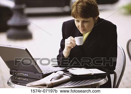 Businesswoman holding a cup of coffee looking at a laptop View Large Photo Image Stock Image - Businesswoman holding a cup of coffee looking at a laptop. Fotosearch