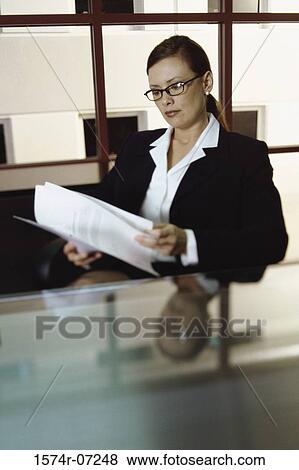 Stock Photo - Businesswoman seated at an office desk reading papers. Fotosearch